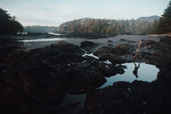Solo person exploring the beach with a beautiful backdrop of forest and ocean in Ucluelet, BC.